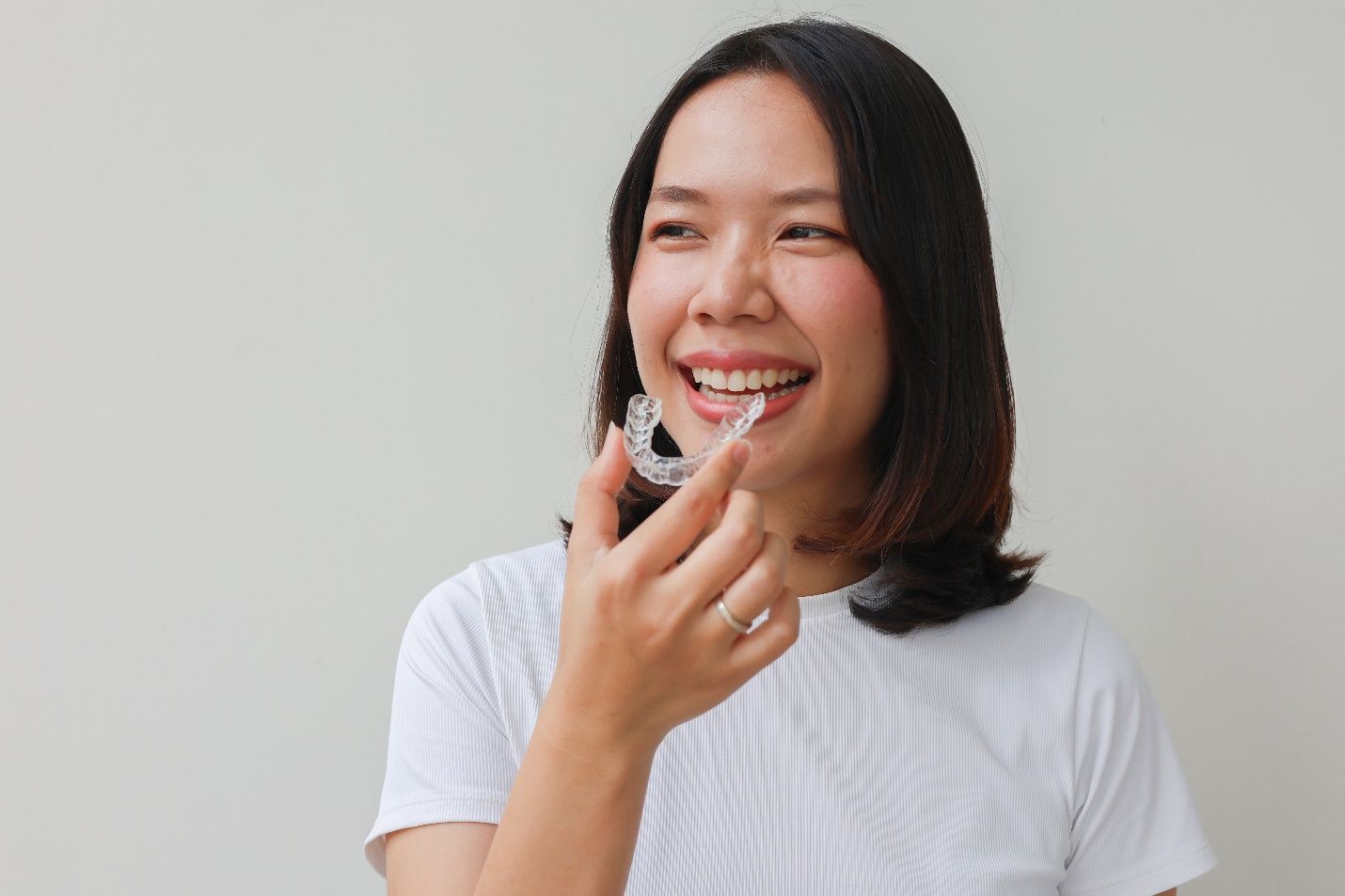 Smiling patient holding clear aligner