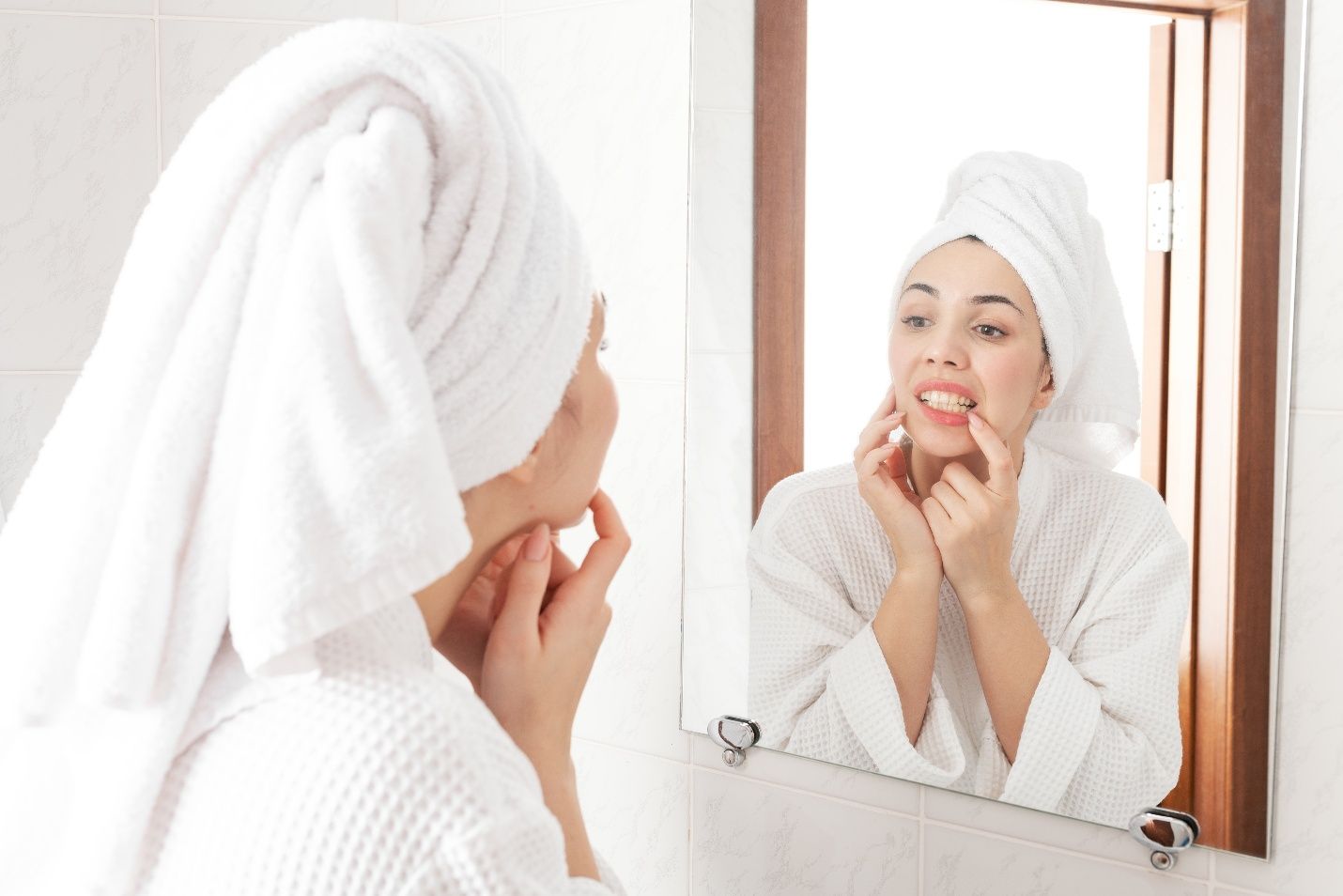 Woman in white robe looking at gums in reflection